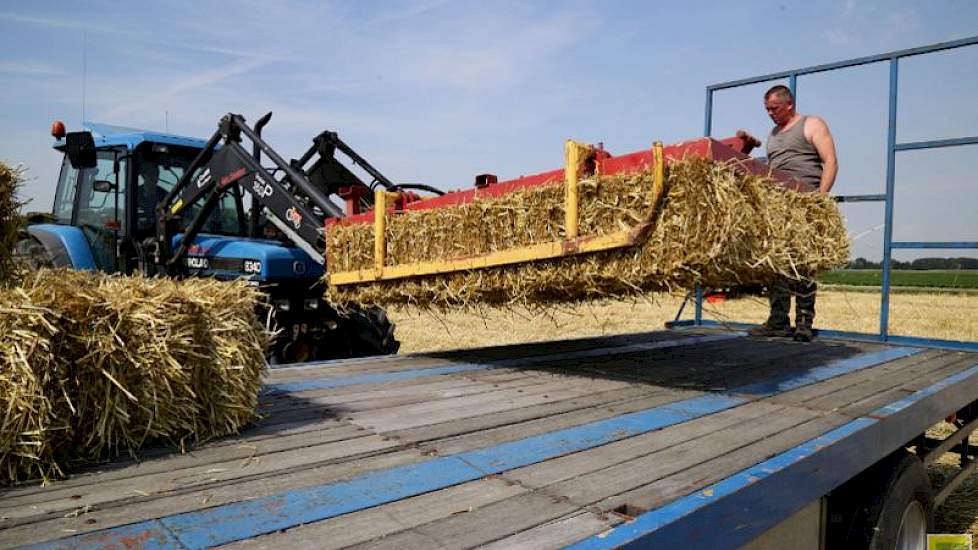 Peter pakt de balen met de knijper en Henri legt ze goed op de wagen.