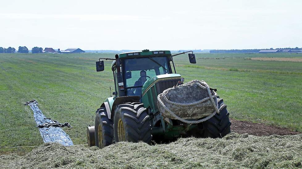 De rollen kuilplastic worden met de trekker de 5 meter hoge kuil opgetrokken.