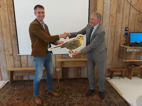 Gedeputeerde Hoogland (rechts ) ontvangt als afsluiting van het herstelproject een geelgors uit handen van Wiebe Bouma, directeur Landschapsbeheer Friesland.