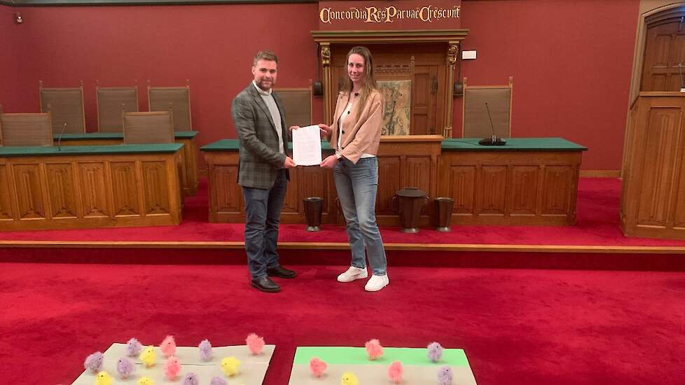 Elisabeth Jukema overhandigt de brandbrief aan gedeputeerde Abel Kooistra. Op de voorgrond links visualisering bezetting gangbare vleeskuikens, rechts de 1 ster Beter Leven vleeskuikens.